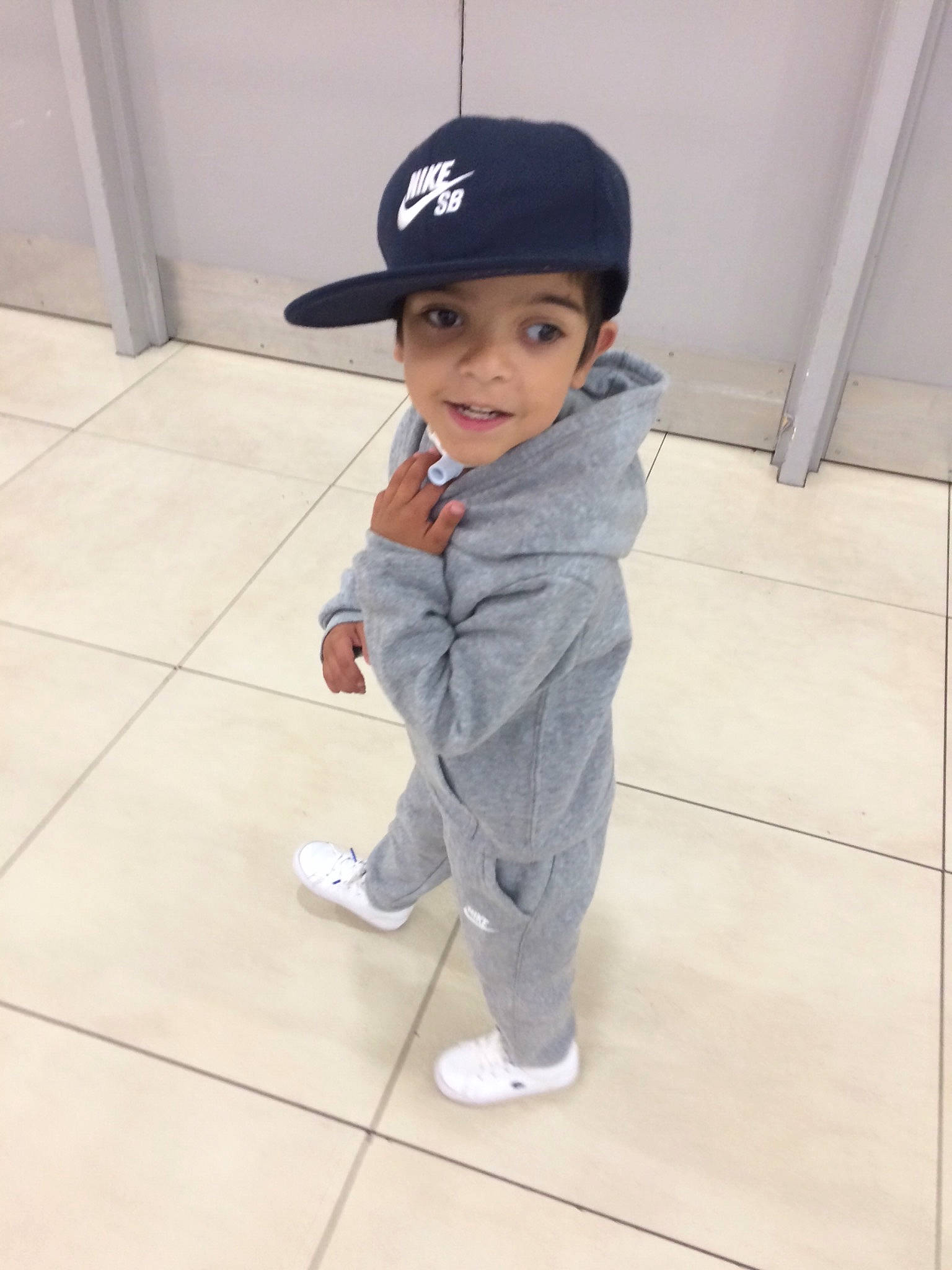 Markis is registered to the contest to win money with this photo: baby, baseball_cap, cap, child, floor, flooring, headgear, headwear, leg, male, person, sleeve, smile, standing, toddler