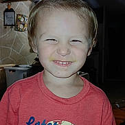 Everett is registered to the contest to win money with this photo: alligator_graphic, casual_clothing, child, cute, face, funny_expression, hair_ponytail, happy, home, indoor, kid, light, person, portrait, red_shirt, smiling, squinting, toddler, tshirt, young_child