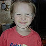 alligator_graphic, casual_clothing, child, cute, face, funny_expression, hair_ponytail, happy, home, indoor, kid, light, person, portrait, red_shirt, smiling, squinting, toddler, tshirt, young_child