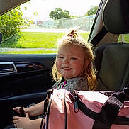 Maelynn joined the competition — help win amazing prizes! child, car_interior, seat, smile, hair, sunlight, window, plastic_bag, pink_bag, clothing, seatbelt, portrait, happy, person, daylight, hair_tie, hand, car_door, greenery, outside_view