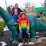 Maelynn joined the competition — help win amazing prizes! boots, bushes, child, colorful_clothing, dinosaur_statue, fun, gas_station, outdoor, person, playful, rainbow_jacket, road, sidewalk, sign, snow, statue, suburban, tongue_out, trees, winter