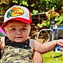 baby, child, hat, cap, camouflage, overalls, outdoor, sunlight, smile, fist, person, playground, greenery, blurred_background, summer, daylight, cute, holding, happy, infant