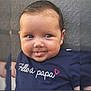 baby, child, face, smile, tongue_out, blue_shirt, text_on_clothing, heart_symbol, closeup, portrait, cute, happy, infant, person, skin, head, eyes, hair, sitting, indoors