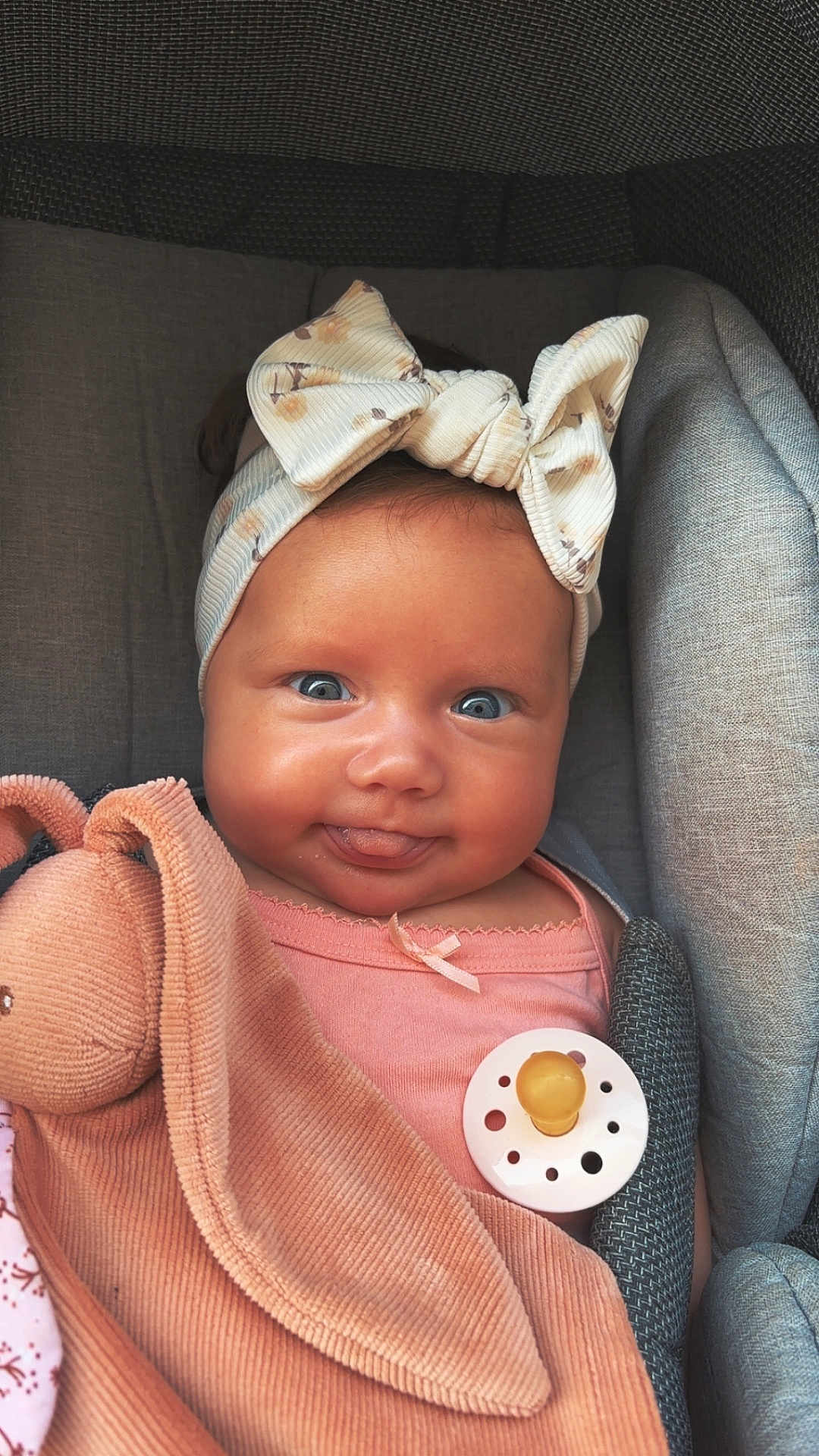 Lolie a rejoint le concours — aidez-le/la à gagner de superbes lots ! baby, child, blue_eyes, bow_headband, pink_clothing, pacifier, plush_toy, bunny, smiling, tongue_out, cute, infant, soft_texture, cushioned_seat, portrait, close_up, indoors, happy, headwear, skin