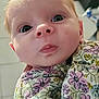 baby, child, close_up, curly_hair, cute, expression, face, floral_clothing, head, human, indoor, infant, newborn, person, portrait, skin, small_hands, soft_light, tongue, wide_eyes