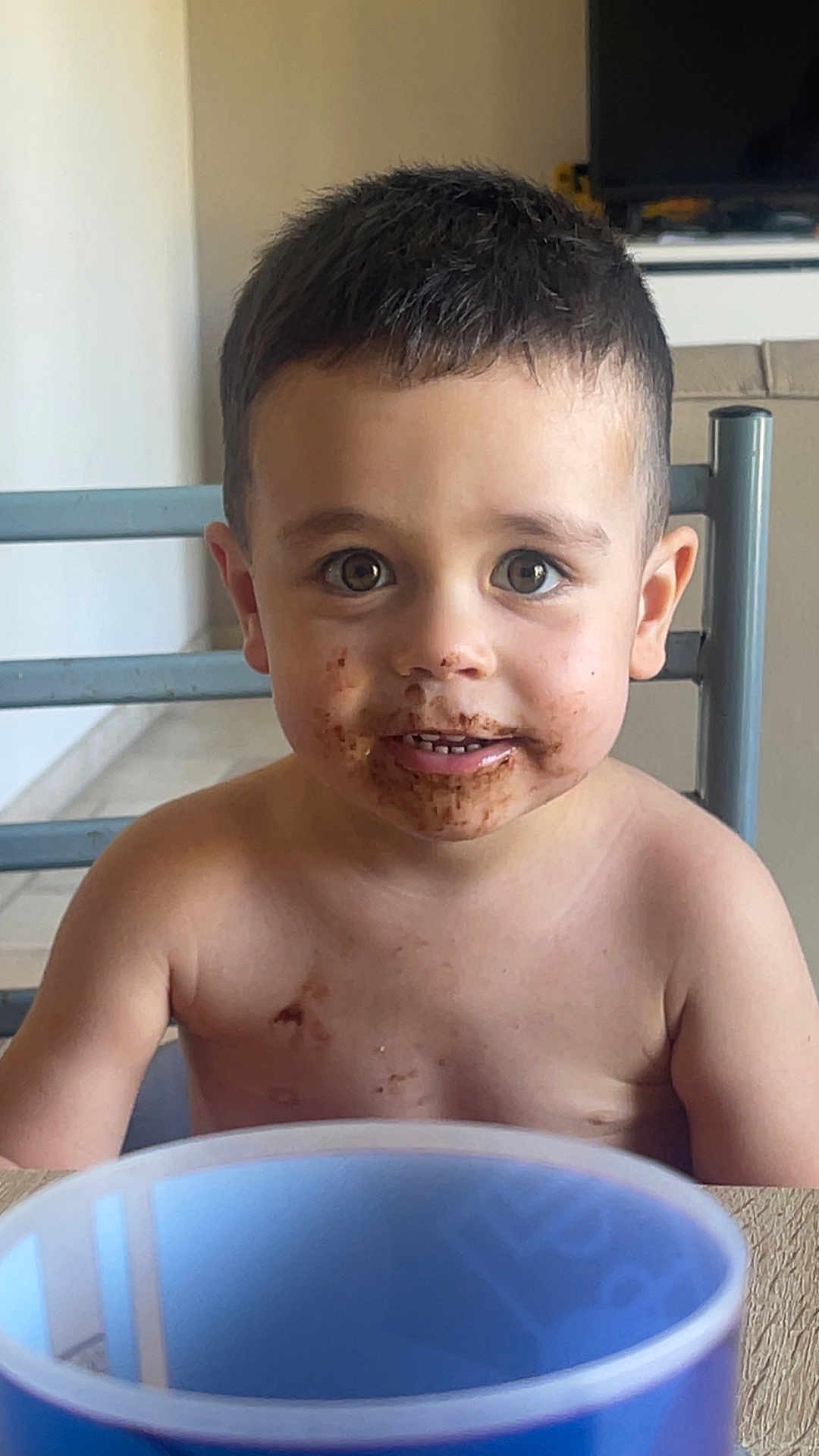 Milo participe au concours pour gagner de l'argent avec cette photo : child, toddler, chocolate, messy, mouth, shirtless, cup, table, indoor, face, eyes, hair, skin, chair, background, expression, portrait, young, curious, smile