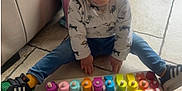 Milo participe au concours pour gagner de l'argent avec cette photo : toddler, child, smiling, indoor, floor, toy, wooden_toy, numbers, colorful, jeans, shirt, sneakers, backpack, couch, tile_floor, play, happy, person, sitting, footwear
