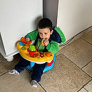 Milo participe au concours pour gagner de l'argent avec cette photo : toddler, child, baby_seat, toy, toy_phone, green_hoodie, blue_seat, indoor, floor_tiles, snack, bread, dinosaur_hoodie, candid, playing, sitting, young_child, person, cute, casual, home