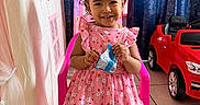 Jasmeen is registered to the contest to win money with this photo: child, girl, pink_dress, smiling, indoor, toy_car, play_tent, chair, curtains, hair_buns, bows, tile_floor, white_shoes, packet, happy, cute, portrait, young_child, home, playtime