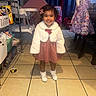 Jasmeen is registered to the contest to win money with this photo: toddler, child, indoor, smiling, dress, white_jacket, flower_hair_clip, tile_floor, high_chair, pink_tent, toy_car, purple_jacket, chair, socks, shoes, furniture, playroom, happy, person, curtains