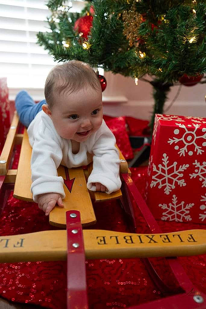 Christina is registered to the contest to win money with this photo: baby, baby_toddler_clothing, child, christmas, christmas_decoration, christmas_eve, christmas_ornament, christmas_tree, event, happy, holiday, holiday_ornament, ornament, person, red, sitting, smile, snapshot, toddler, tree