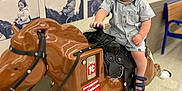 Timothy is registered to the contest to win money with this photo: toddler, child, mechanical_horse, ride, coin_operated, indoor, floor, bench, wall, photos, black_and_white, portrait, serious, shorts, shirt, sandals, toy, play, kid, amusement