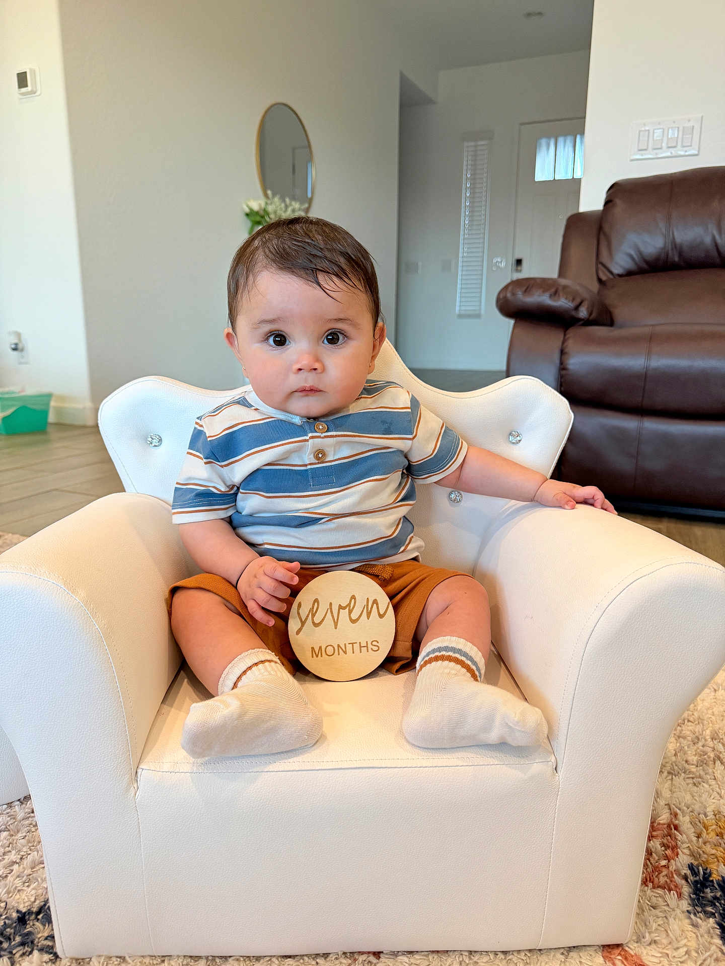 Aavyan Sapkota joined the competition — help win amazing prizes! baby, child, infant, armchair, white_chair, wooden_sign, seven_months, striped_shirt, socks, brown_shorts, living_room, carpet, leather_sofa, mirror, flowers, flooring, person, indoor, cute, portrait