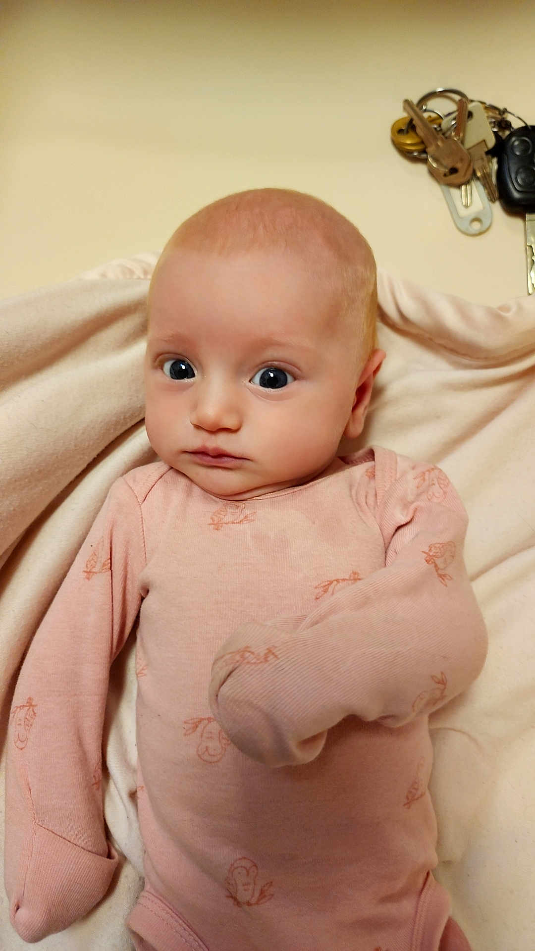 Raelynn joined the competition — help win amazing prizes! baby, infant, pink_onesie, blanket, face, wide_eyes, mittened_sleeves, person, portrait, indoor, keys, wall, curious, soft_lighting, newborn, clothing, cute, child, human, cozy