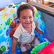 Thelio a rejoint le concours — aidez-le/la à gagner de superbes lots ! child, clothing, colorful, curly_hair, eyes, face, fun, hand, happy, indoor, inflatable, mouth, plastic, playful, seat, shorts, smiling, striped_shirt, toddler, toy