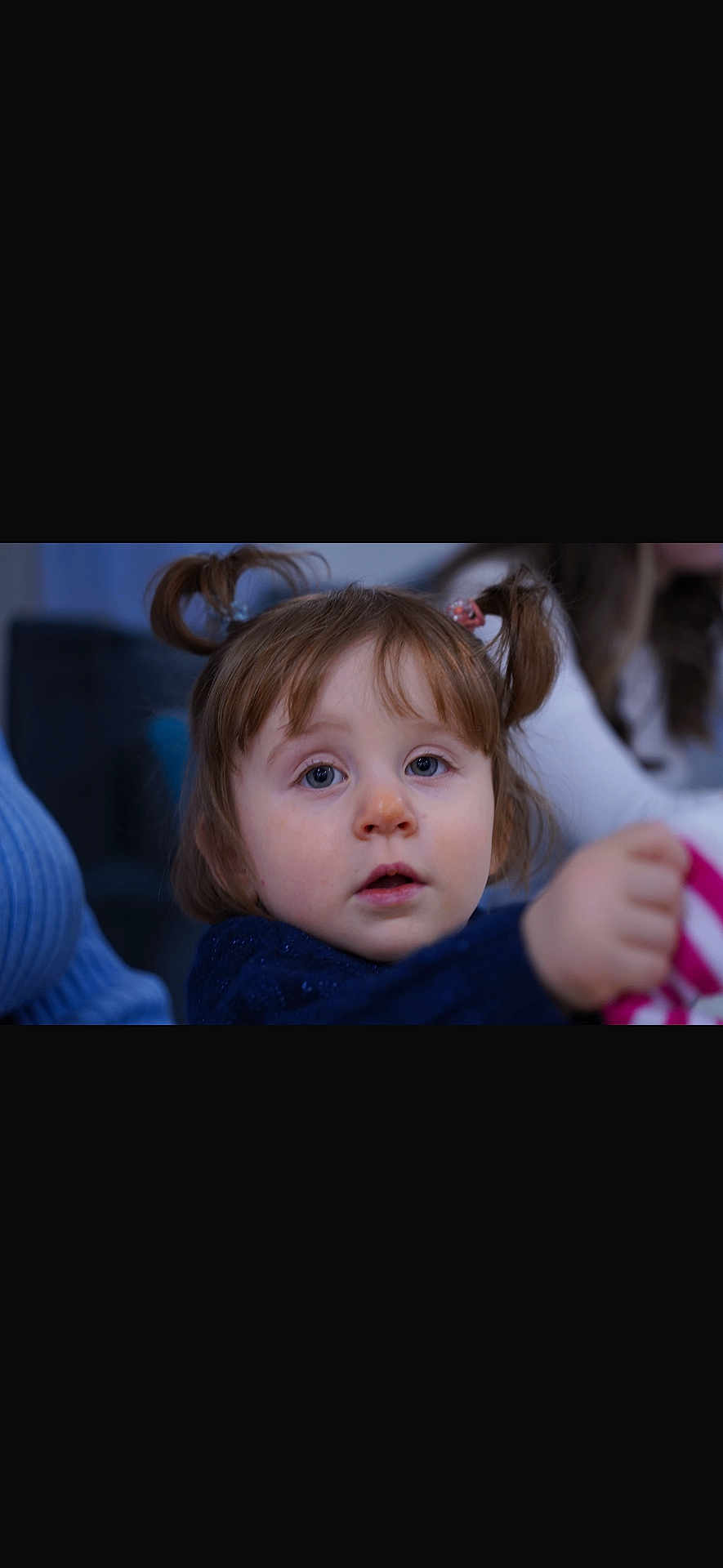 Elena participe au concours pour gagner de l'argent avec cette photo : toddler, child, portrait, face, blue_eyes, pigtails, hair, sweater, toy, hand, indoors, couch, blurred_background, candid, curious_expression, sitting, parent, soft_lighting, closeup, surprised
