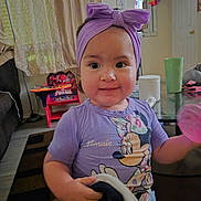 Mia joined the competition — help win amazing prizes! baby, child, infant, smiling, portrait, indoors, purple_headband, bow, purple_shirt, cartoon_shirt, toy, spiderman, pink_pom_pom, living_room, table, chair, curtains, door, mirror, home_decor