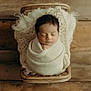 newborn, baby, sleeping, wrapped, blanket, wicker_basket, wooden_floor, cozy, peaceful, infant, soft_texture, portrait, indoors, cute, child, resting, closeup, warm_tones, head, hands
