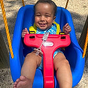 Zain joined the competition — help win amazing prizes! baby, child, swing, playground, smile, happy, outdoor, sunlight, blue_swing, yellow_straps, infant, legs, feet, red_safety_bar, pacifier, tree, gravel, play_equipment, cute, fun