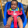 baby, child, swing, playground, smile, happy, outdoor, sunlight, blue_swing, yellow_straps, infant, legs, feet, red_safety_bar, pacifier, tree, gravel, play_equipment, cute, fun