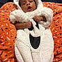 baby, child, costume, ghost, white, orange_blanket, cute, surprised, hooded, fluffy, infant, patterned_blanket, lying_down, indoor, portrait, soft_texture, hands, face, expression, holiday
