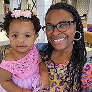V'Niyah is registered to the contest to win money with this photo: braids, casual, chair, child, colorful_clothing, cute, family, glasses, hair_accessories, happy, holding, indoor, person, pink_dress, portrait, restaurant, smile, table, toddler, woman