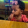 toddler, child, girl, hair_accessory, pink, snack, table, wood, indoor, restaurant, bar, chair, curly_hair, portrait, person, casual_clothing, cute, eating, side_view, young_child