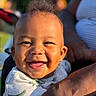 adult, baby, child, close_up, clothing, earrings, eyes, face, hair, holding, infant, laughing, onesie, outdoor, parent, portrait, smiling, sunlight, teeth, topknot