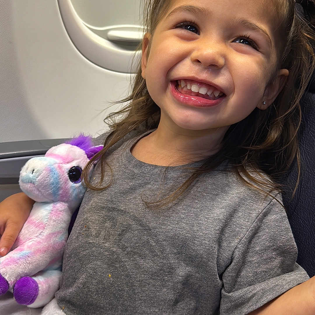 Sienna is registered to the contest to win money with this photo: bodypart, child, clothing, cushion, face, female, girl, happy, head, homedecor, laughing, mouth, person, photography, plush, portrait, smile, t_shirt, teeth, toy