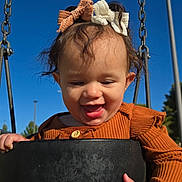 Zeyleea is registered to the contest to win money with this photo: toddler, child, swing, playground, outdoor, happy, smiling, bow, hair_accessory, sunlight, blue_sky, clothing, rust_color, face, hand, person, daylight, joyful, park, fun