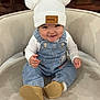 Alizeth is registered to the contest to win money with this photo: apparel, baby, boots, chair, child, clothing, comfortable, cute, denim_overalls, face, happy, hat, indoor, infant, person, pom_poms, portrait, sitting, smile, white_shirt