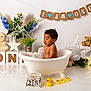 baby, bathtub, bubbles, celebration, child, decorations, duck, first_birthday, flowers, indoor, light, plant, rubber_duck, smiling, star_lights, teddy_bear, toy, water, white_background, young_child