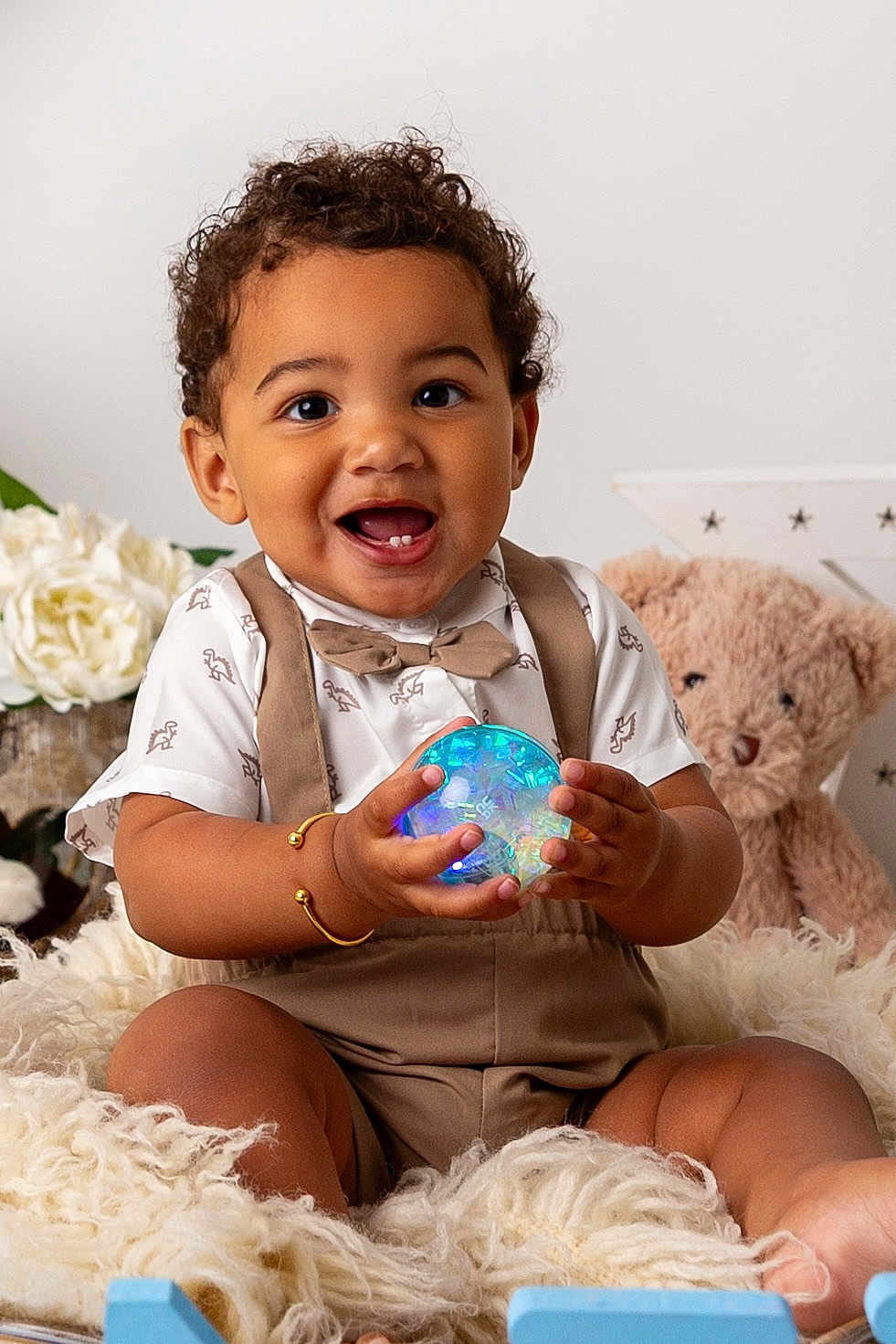 Dejai joined the competition — help win amazing prizes! baby_bracelet, bow_tie, child, close_up, curly_hair, cute, dinosaur_pattern, fluffy_blanket, glowing_orb, happy, holding_object, indoor, person, portrait, seated, smiling, suspenders, teddy_bear, toddler, white_flowers