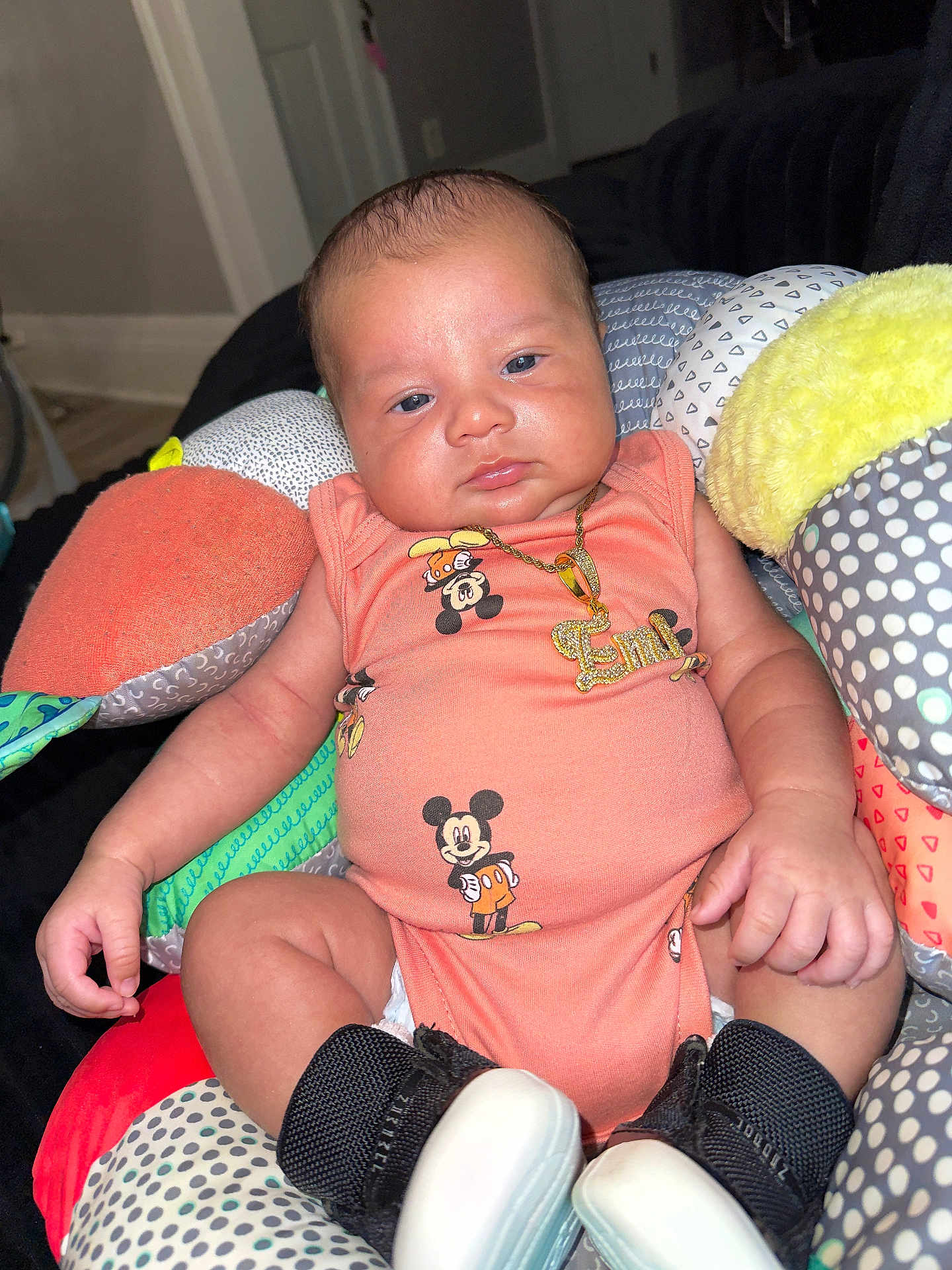 Emiliano joined the competition — help win amazing prizes! baby, infant, mickey_mouse, onesie, necklace, sneakers, cushion, patterned, colorful, indoor, person, child, cute, fashion, jewelry, footwear, relaxed, portrait, small, seated