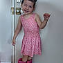child, girl, pink_dress, rain_boots, winking, smiling, standing, indoors, door, wooden_floor, hair_clips, playful, posing, white_wall, flooring, cute, person, fashion, happy, casual