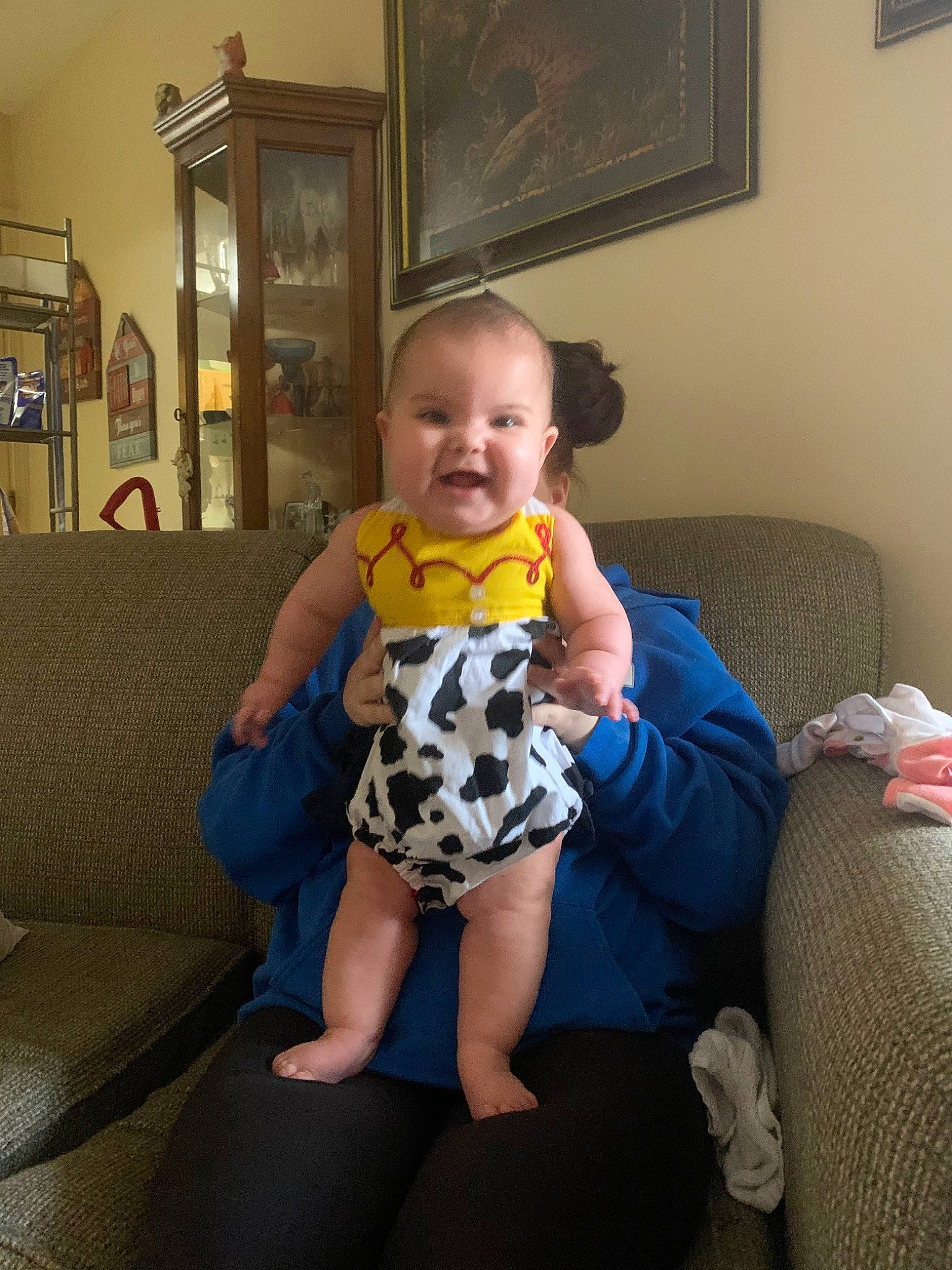 Indigo is registered to the contest to win money with this photo: baby, baby_toddler_clothing, comfort, couch, dress, electric_blue, floor, flooring, fun, happy, human_leg, knee, lap, living_room, person, picture_frame, room, sitting, smile, thigh