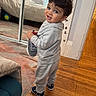 toddler, child, indoor, wooden_floor, tracksuit, shoe, playful, curious, person, mirror, carpet, lamp, sofa, sticker, wall, head, hair, smile, footwear, home