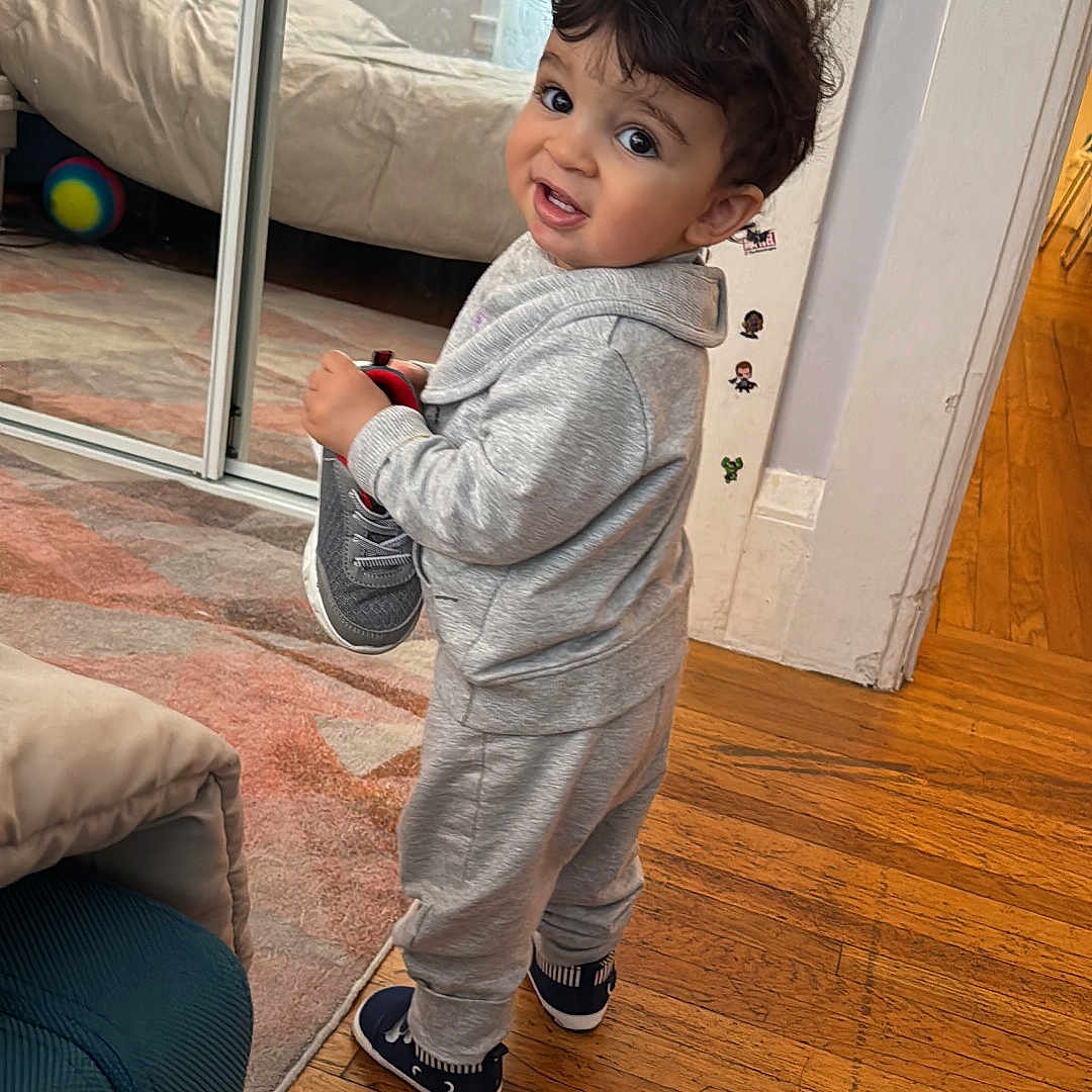 Amir joined the competition — help win amazing prizes! toddler, child, indoor, wooden_floor, tracksuit, shoe, playful, curious, person, mirror, carpet, lamp, sofa, sticker, wall, head, hair, smile, footwear, home