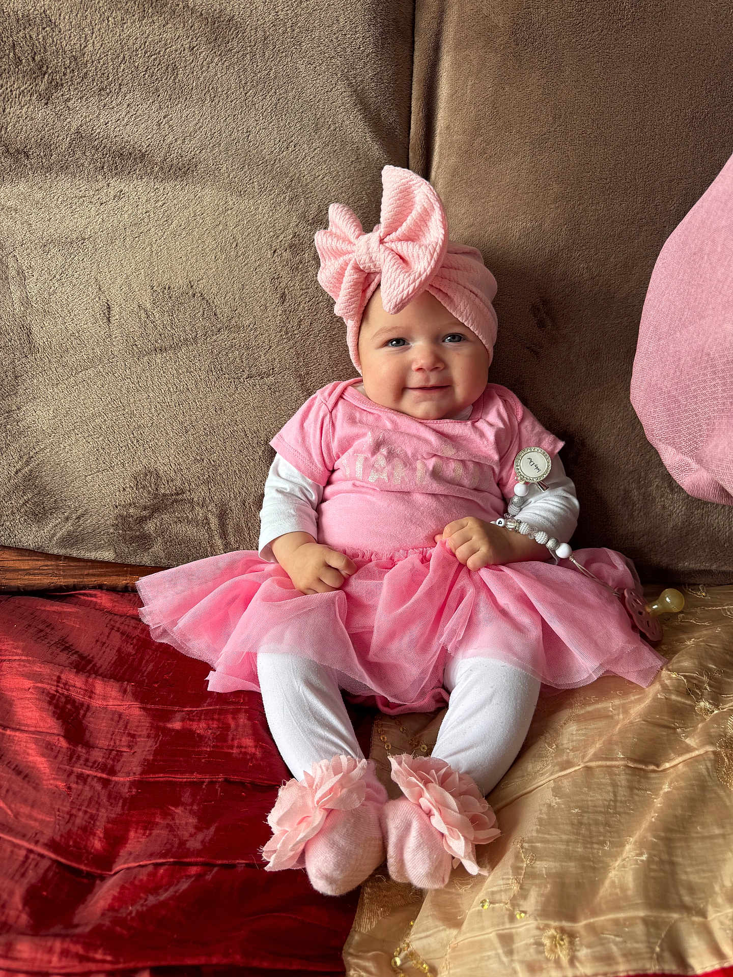 Paula participe au concours pour gagner de l'argent avec cette photo : baby, pink, tutu, headwrap, pacifier, couch, smile, sitting, cute, child, indoors, soft_toys, clothing, footwear, face, person, infant, fabric, home, accessory