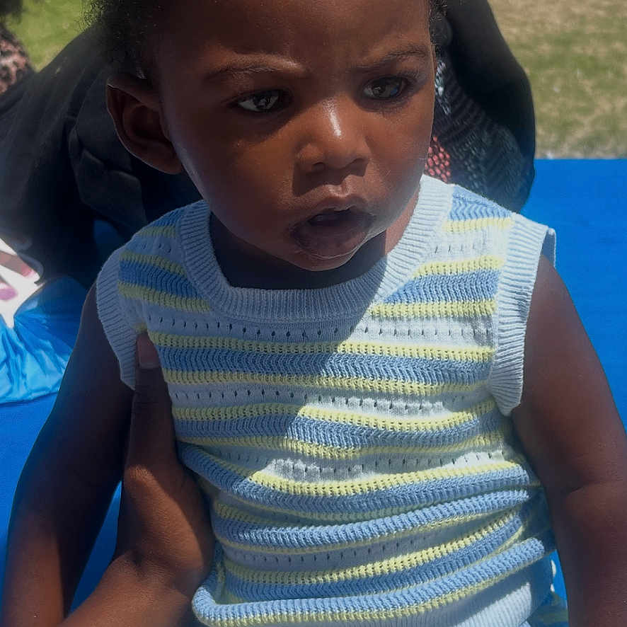 Brycyn joined the competition — help win amazing prizes! toddler, child, outdoor, knitted_clothing, striped, blue, grass, hand, person, serious_expression, summer, sunlight, shorts, sitting, young_child, curly_hair, baby, daylight, park, support