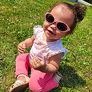 Sinay a rejoint le concours — aidez-le/la à gagner de superbes lots ! child, toddler, grass, outdoor, sunlight, sunglasses, pink_clothing, curly_hair, smiling, sitting, summer, nature, footwear, cute, happy, playful, baby, greenery, casual, daylight