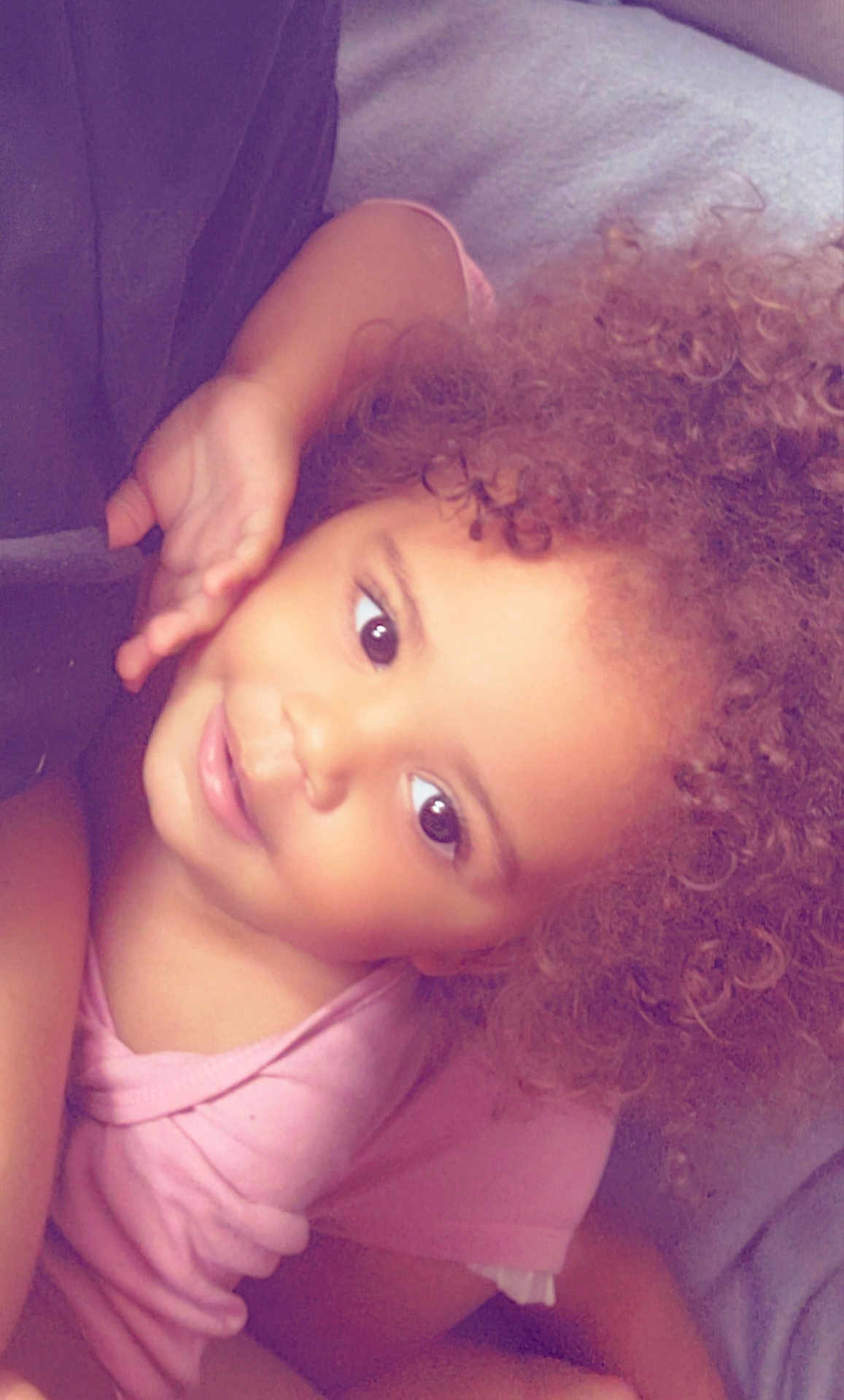 Ashanti participe au concours pour gagner de l'argent avec cette photo : child, toddler, curly_hair, pink_shirt, smile, face, eyes, skin, hand, laying_down, portrait, cute, indoors, comfort, happy, baby, person, young_child, head, expression