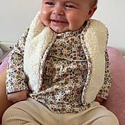 Ambre participe au concours pour gagner de l'argent avec cette photo : baby, infant, smiling, sitting, floral_pattern, sherpa_vest, long_sleeve, pants, socks, blanket, bed, portrait, chubby_cheeks, hair, rosy_cheeks, hands, feet, cozy, indoor, cute