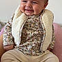 baby, infant, smiling, sitting, floral_pattern, sherpa_vest, long_sleeve, pants, socks, blanket, bed, portrait, chubby_cheeks, hair, rosy_cheeks, hands, feet, cozy, indoor, cute