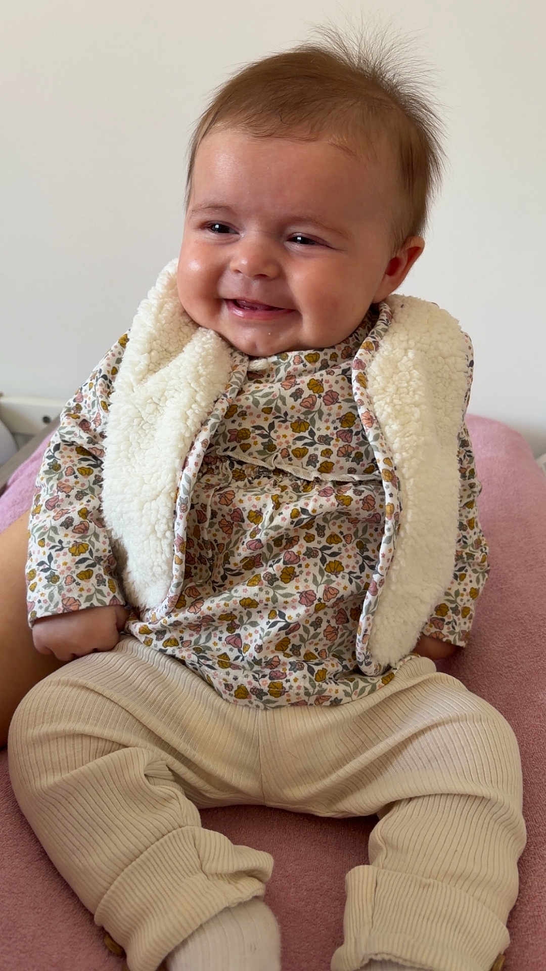 Ambre participe au concours pour gagner de l'argent avec cette photo : baby, infant, smiling, sitting, floral_pattern, sherpa_vest, long_sleeve, pants, socks, blanket, bed, portrait, chubby_cheeks, hair, rosy_cheeks, hands, feet, cozy, indoor, cute
