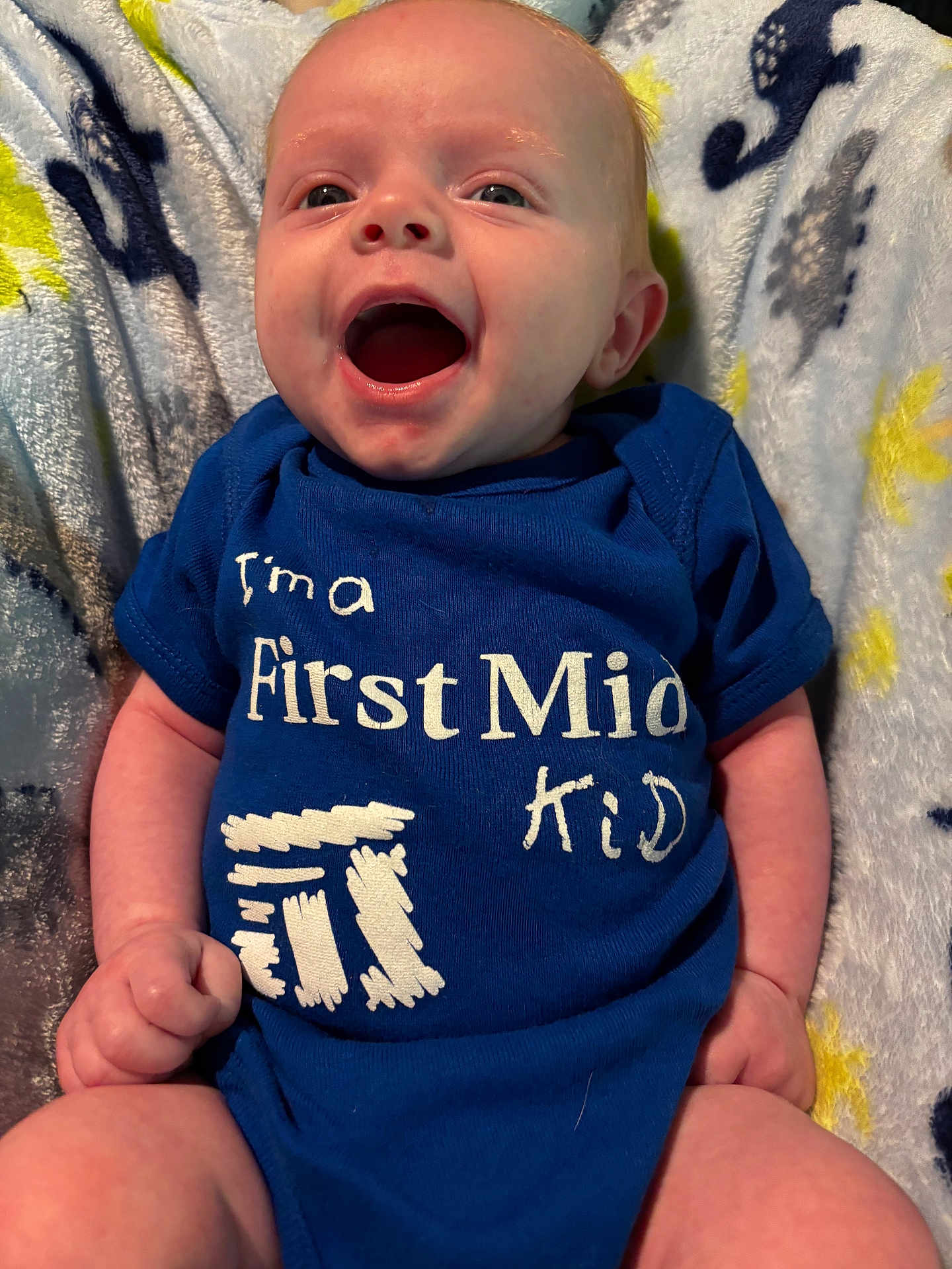 Kynxton joined the competition — help win amazing prizes! baby, infant, smiling, blue_onesie, text_on_clothing, blanket, happy, child, cute, face, mouth_open, lying_down, skin, hand, legs, indoors, soft_texture, patterned_blanket, young_child, portrait