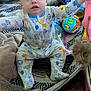 baby, child, pajamas, animal_print, blanket, toy, floor, wood_floor, indoor, person, sitting, reaching, colorful, face, foot, patterned_rug, soft_toys, expression, curious, home