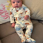 Andrew joined the competition — help win amazing prizes! baby, infant, onesie, dinosaur_pattern, couch, pillow, embroidery, cozy, child, cute, indoor, portrait, clothing, comfortable, relaxed, curious, furniture, soft, home, seated