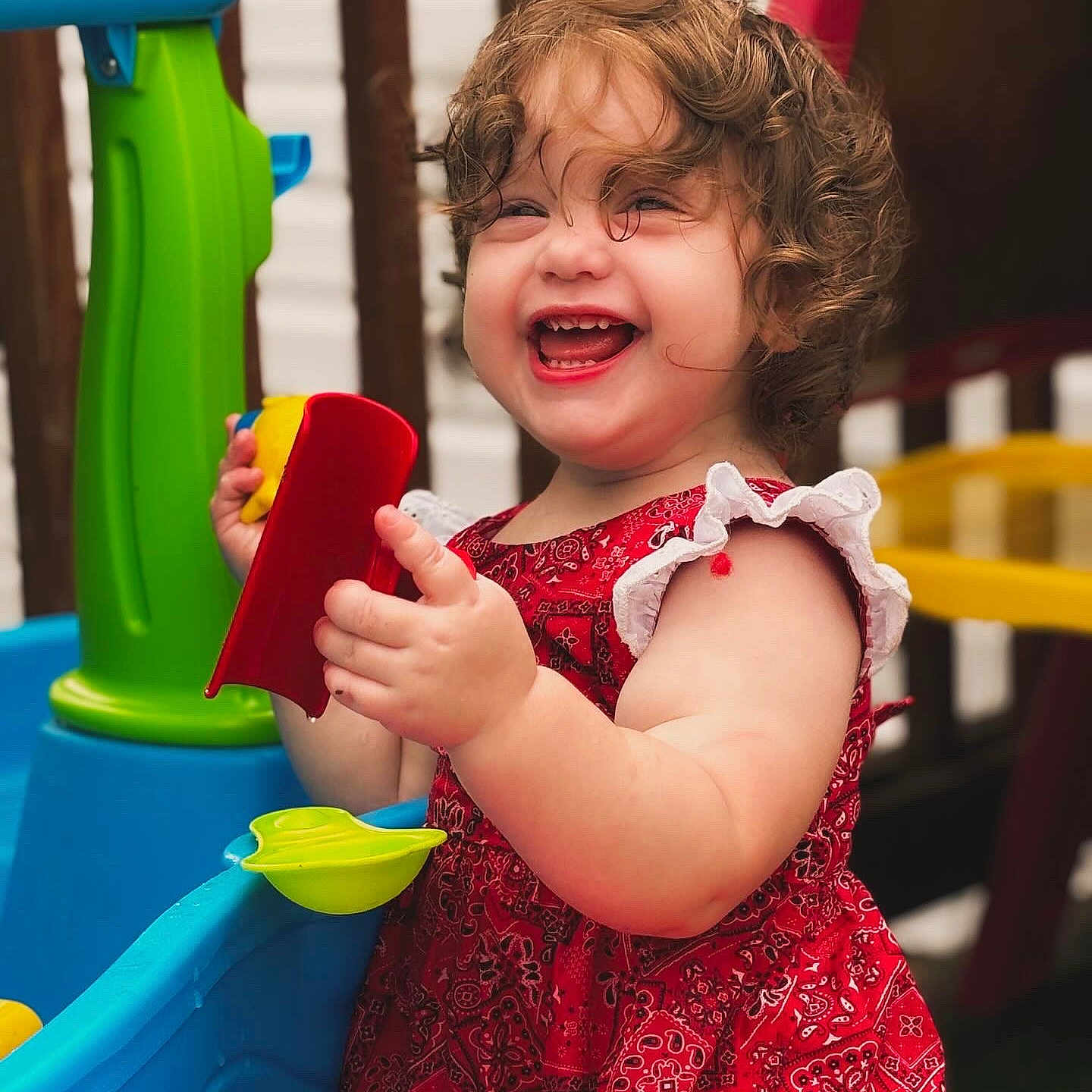 Gabriella is registered to the contest to win money with this photo: baby, clothing, dress, face, happy, head, laughing, outdoors, person, photography, pingpong, pingpongpaddle, plant, playarea, portrait, pottedplant, racket, smile, sport, summer