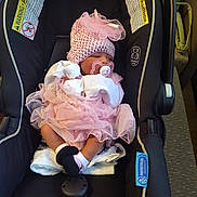 Naomi is registered to the contest to win money with this photo: baby, infant, car_seat, pink_clothing, hat, pacifier, socks, blanket, sleeping, indoors, safety_warning, infant_carrier, newborn, cute, tulle_skirt, child, resting, protectplus, snugride, seat_belt